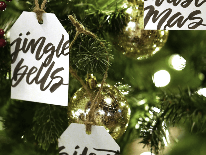 Christmas tags decorated with calligraphy lettering hanging from a christmas tree